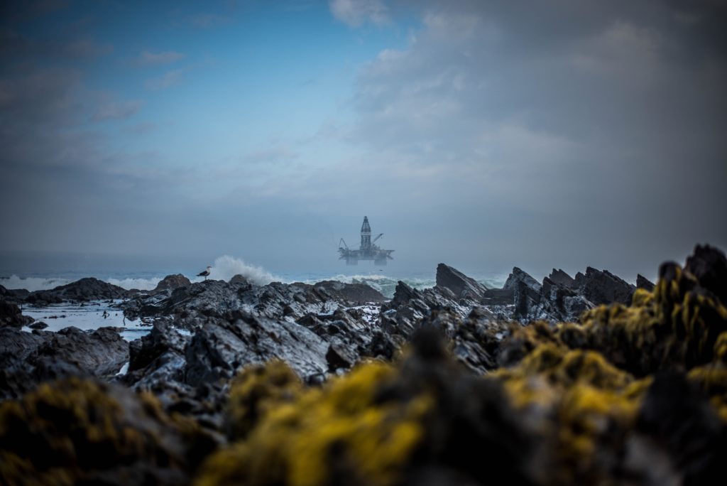 View of an oil rig at sea, with rocks close by