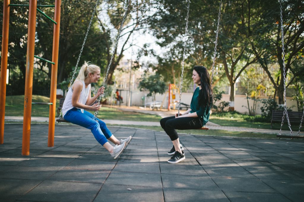 Two people on swings facing each other and having an animated conversation