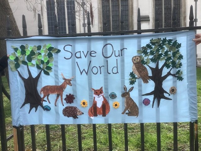 A protester's banner on railings, saying "Save Our World" with pictures of trees, flowers and animals