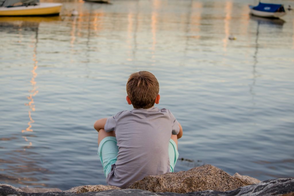 A child sitting regarding a calm expanse of water