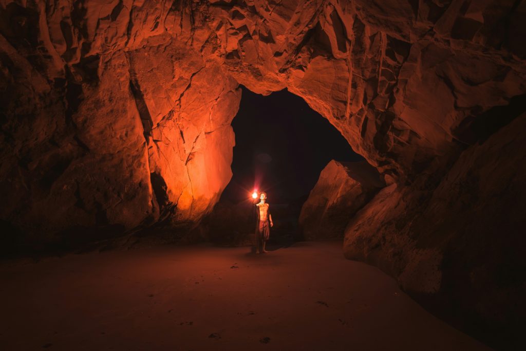 A person alone in a dark cave with a single lamp