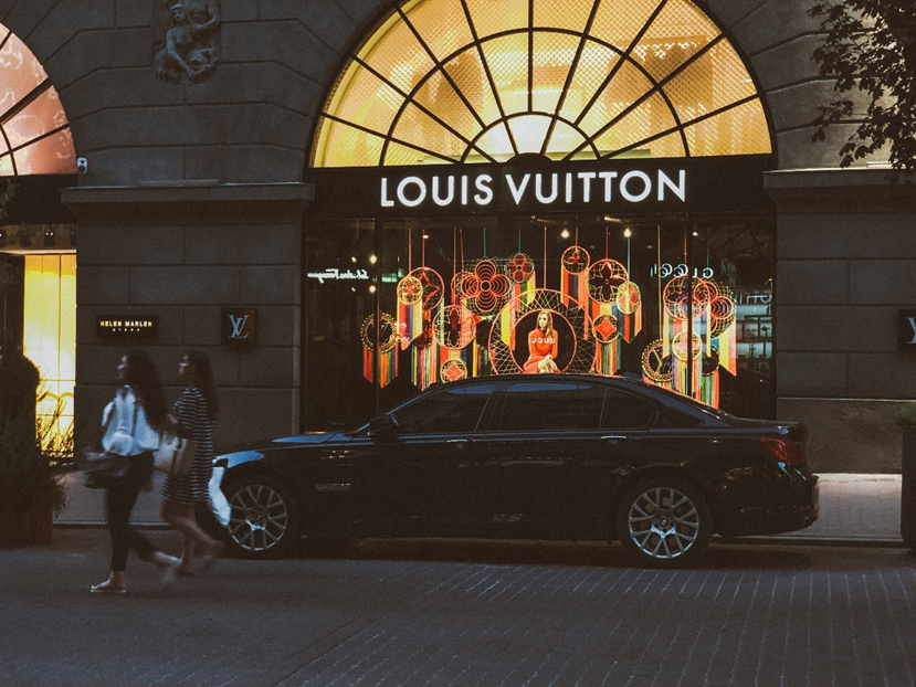 A Louis Vuitton shop glowing with temptation, and an expensive car outside